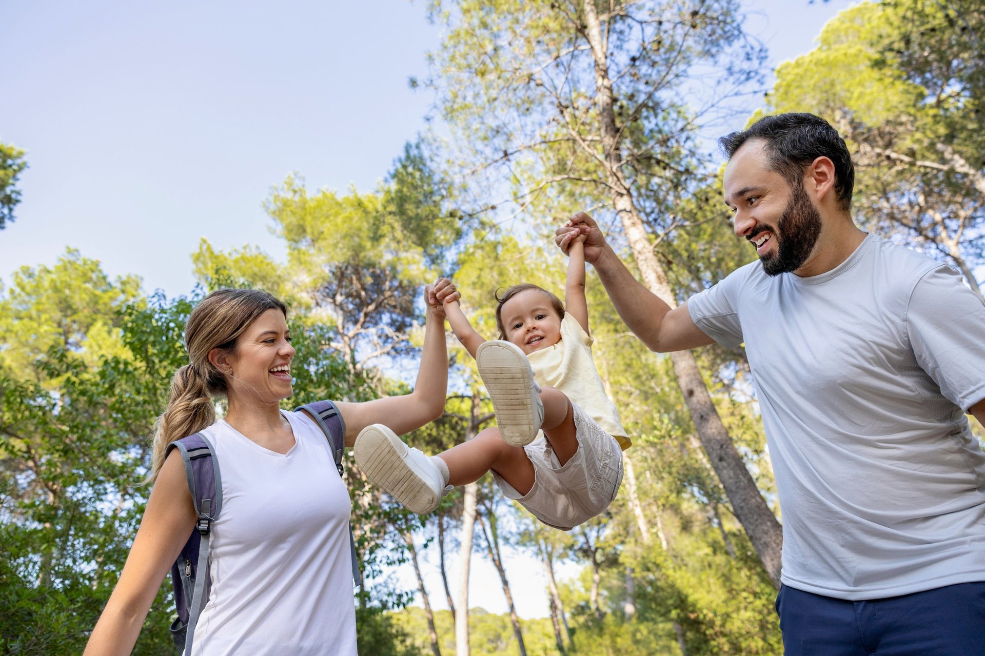 Smiling toddler plays joyfully with her parents in a sunny forest path